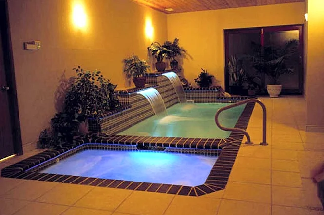 Indoor Cyberlane pool and spa with the room lights on and plants around the tile edge