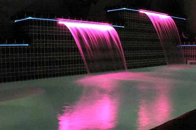 Sheer Descent waterfalls lit pink by fiber optic lighting in an indoor pool