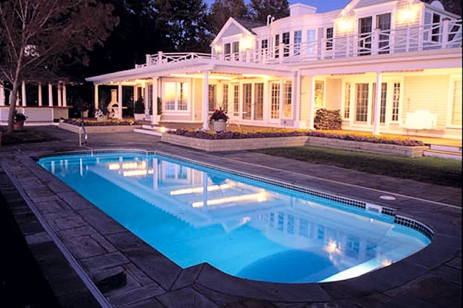 The pool lit at dusk in front of the big white house