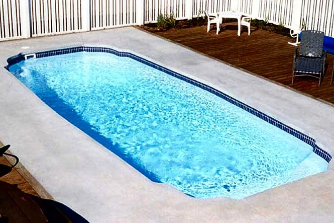 The pool beside a wood deck and concrete deck, with a white fence