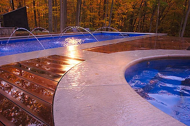 Deck jets arcing into the pool beside curved coping and the wood deck