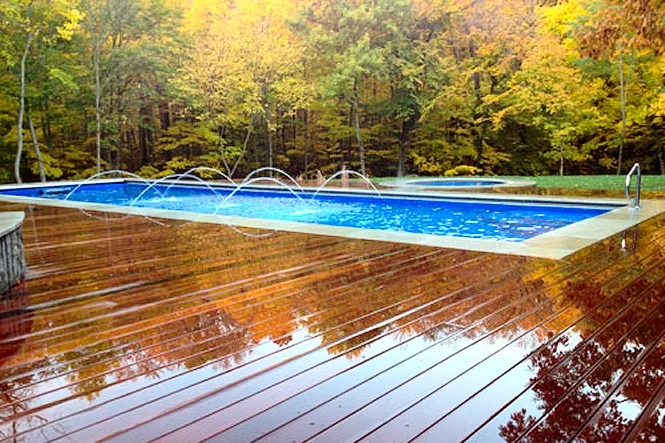 Wet wood deck reflecting the autumn trees beside the pool