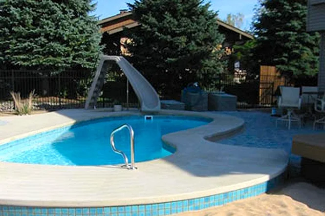 Pool, slide and sand beach with the house and trees behind