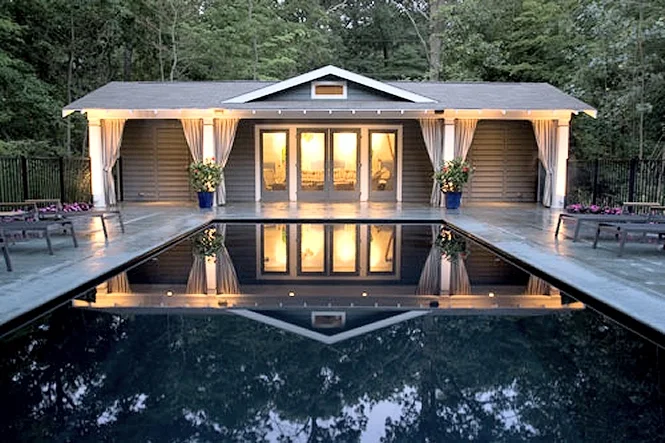 Pool house with lit windows reflected in the dark water of the Monte Carlo pool at dusk
