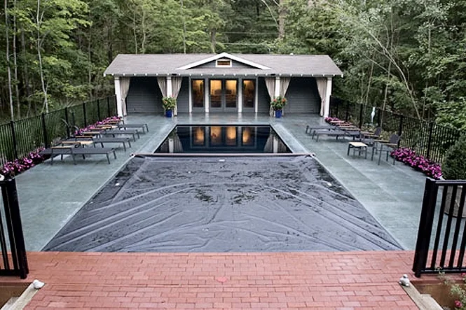 The automatic cover across the pool, seen from the brick patio by the fence