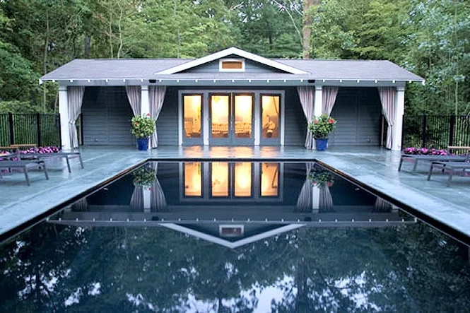 The pool house lit up in the evening behind the dark water of the pool