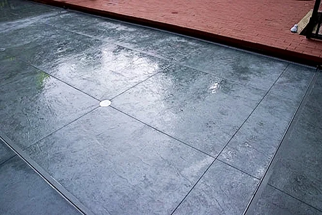 Close view of wet texture-stamped concrete decking beside the pool