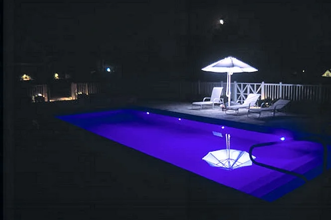 The pool lit deep blue at night under a patio umbrella