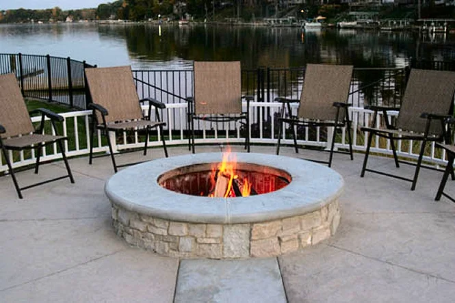 Round stone fire pit with chairs on the deck, the lake behind