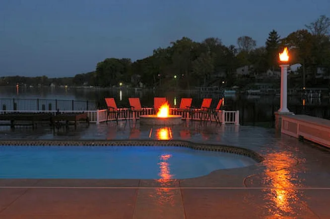 The pool at dusk with the fire pit glowing and the lake beyond