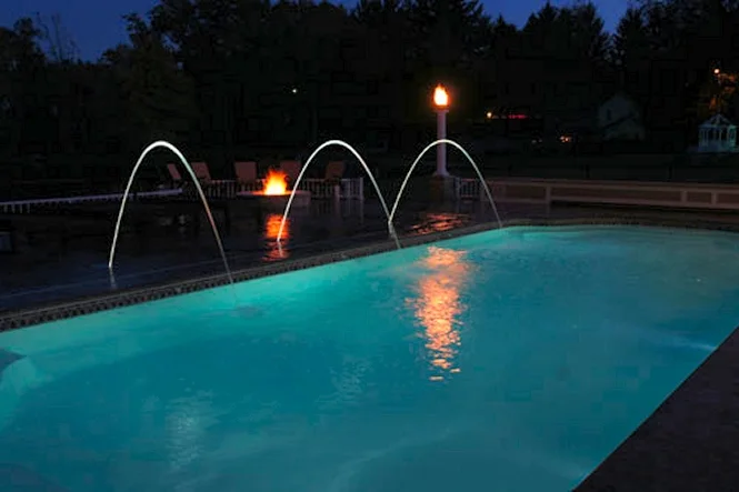 Deck jets arcing into the lit pool at dusk