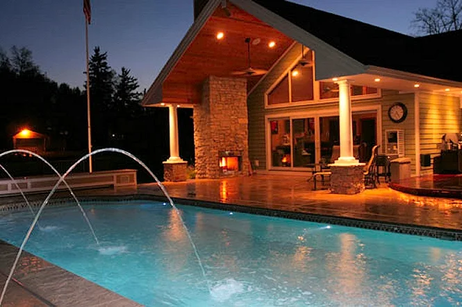 The house porch and stone fireplace lit at night behind the deck jets