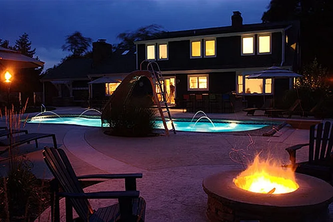 Night view of the lit pool, the fire pit and the house