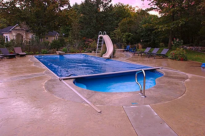 The pool cover partly across the water with the slide behind