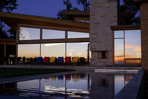Tall windows of the modern house reflected in the pool at dusk