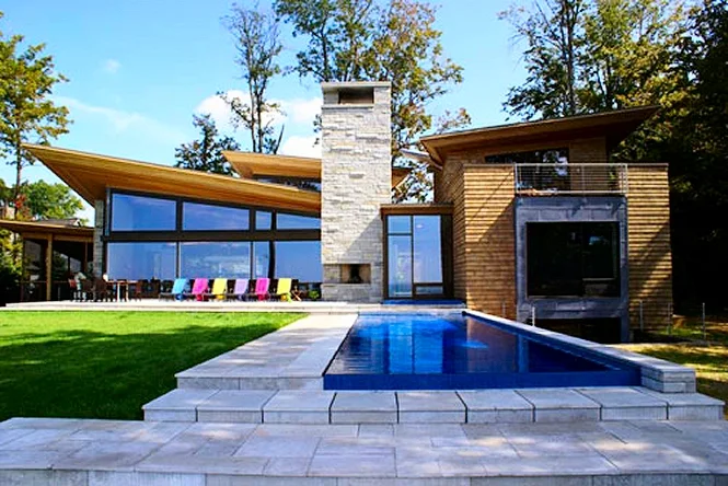 The long pool on the lawn in front of a stone and glass house